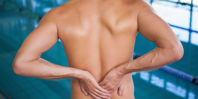 mid section shirtless swimmer with back ache by pool